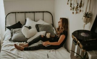 woman lying on a bed with a cup of tea looking thoughtful