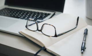 a laptop, notebook and pair of glasses.